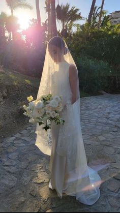 a woman in a wedding dress holding a bouquet and posing for a photo on her cell phone