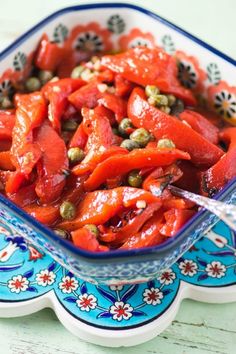 a bowl filled with red peppers and capers on top of a blue and white plate