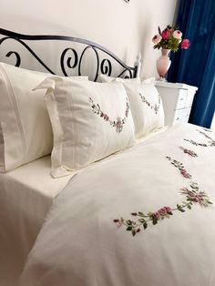 a white bed topped with lots of pillows next to a blue curtain and window sill