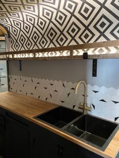 a kitchen with black and white tiles on the wall, wooden counter top and sink