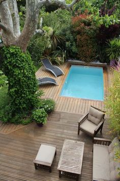 an outdoor deck with lounge chairs and a swimming pool in the middle of it is surrounded by greenery