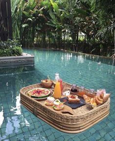 a boat filled with food sitting on top of a pool next to a lush green forest