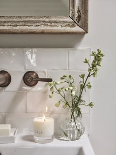 a bathroom sink with a candle and flowers in a vase next to the faucet