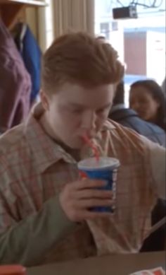 a young boy drinking from a cup while sitting at a table