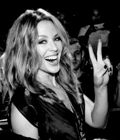 a black and white photo of a woman making the peace sign with her hand at a concert