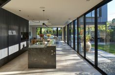 a long hallway with glass walls leading to an outdoor kitchen and dining area, along with potted plants on the far wall