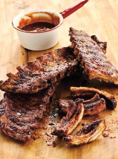 some ribs are on a cutting board with dipping sauce