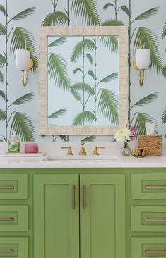 a bathroom vanity with green cabinets and palm leaves on the wall behind it is a mirror