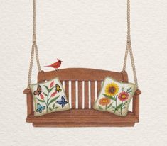 a wooden swing with two pillows hanging from it's sides and a bird sitting on the back