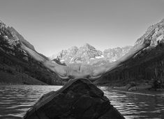 a man laying on top of a rock next to a body of water with mountains in the background