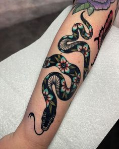 a person with a tattoo on their arm has a snake and flowers tattooed on it