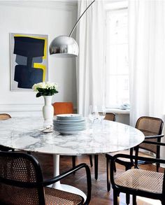 a dining room table with chairs and plates on it in front of a painting hanging from the wall