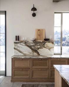 a marble counter top in a kitchen with wooden cabinets and an art piece on the wall