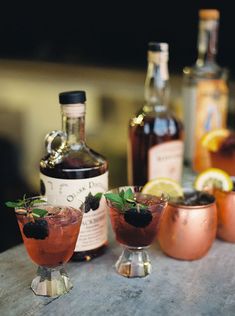 three glasses filled with drinks sitting on top of a table next to bottles and spoons