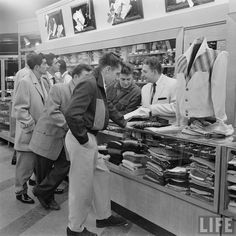 men in suits and ties are looking at items on display inside a store while another man stands near the counter