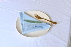 a white plate topped with a blue napkin and gold fork next to a green leaf