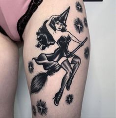 a woman with a witch hat and broom tattoo on her thigh is holding a broom