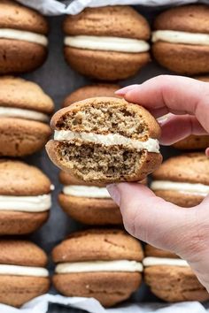 a person holding a cookie sandwich in front of some cookies on a baking sheet with white frosting