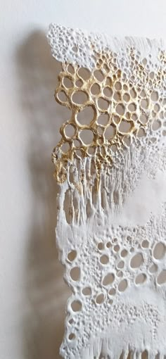 two pieces of white lace with gold rings on them, hanging from the side of a wall