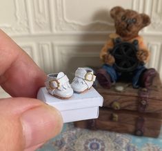 someone is holding a tiny pair of baby shoes in front of a teddy bear sitting on a suitcase