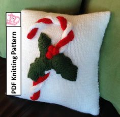 a knitted christmas pillow with candy canes and holly leaves on the front, sitting on a green couch