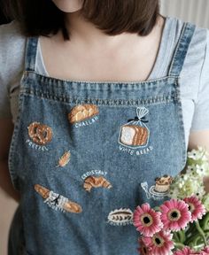 a woman holding a bouquet of flowers and wearing an apron with embroidered patches on it