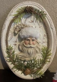 a plate with a santa clause on it and pine cones around the edge, sitting on a table