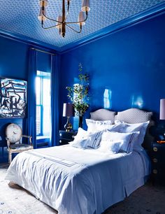 a bedroom with blue walls and white linens on the bed, along with a chandelier