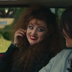 a woman sitting in the back seat of a car talking on a cell phone with another woman standing next to her