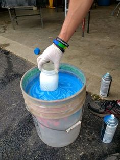 a person in white gloves is pouring blue liquid into a bucket