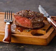 a piece of steak on a cutting board with a knife and fork next to it