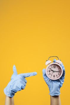 two hands in blue gloves pointing at an alarm clock and pointing to the right with one hand