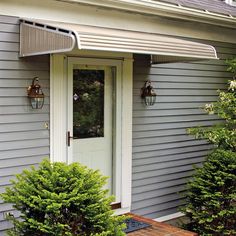 the front door of a gray house with white trim and an awning over it