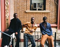 three young men sitting on the steps of a brick building, posing for a photo