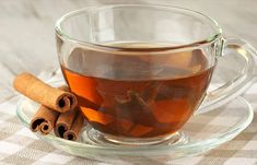 a glass cup filled with tea next to cinnamon sticks