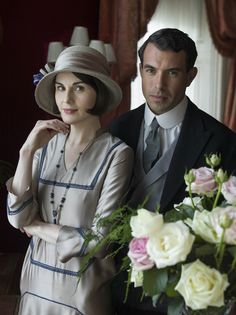 a man and woman standing next to each other in front of a vase with flowers