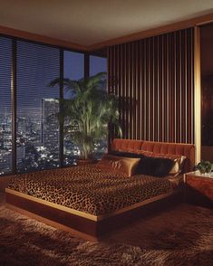 a bedroom with a leopard print bed spread and large windows overlooking the city at night