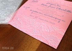 a pink and white wedding card sitting on top of a wooden table next to a plastic box