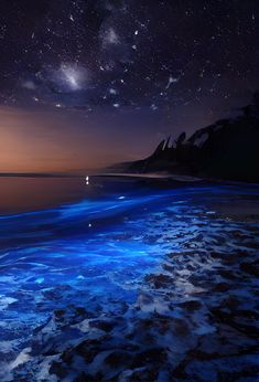 the night sky is lit up with stars and clouds over the ocean as waves roll in