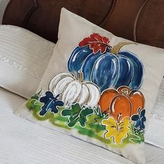 a decorative pillow with pumpkins and leaves painted on it sits on a white bed