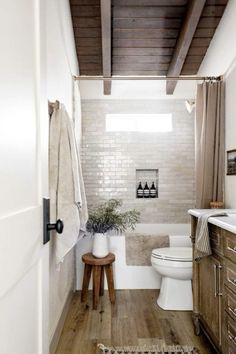 a white toilet sitting next to a bath tub in a bathroom under a wooden ceiling