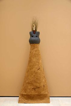 a tall brown vase sitting on top of a white floor next to a wall with a plant growing out of it