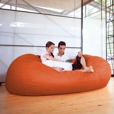 a man and woman sitting on an orange bean bag chair looking at a tablet computer