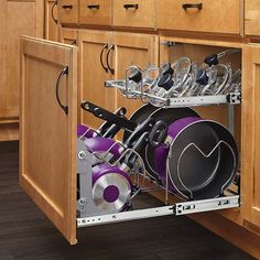 an open kitchen cabinet with pots and pans in the bottom drawer, on wooden flooring