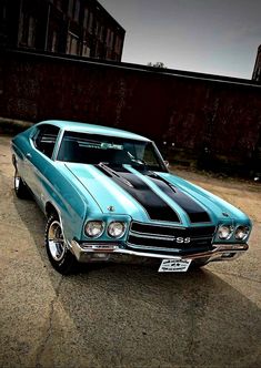 a blue and black muscle car parked in a parking lot next to a brick wall