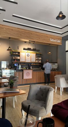 the interior of a coffee shop with chairs and tables in front of it, while a man stands behind the counter