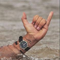 a man with a wrist tattoo holding his hand up in the water while wearing a watch