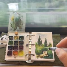 a person holding a paintbrush and an open book with watercolors on it