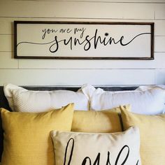 a bed topped with pillows next to a wooden sign that says you are my sunshine