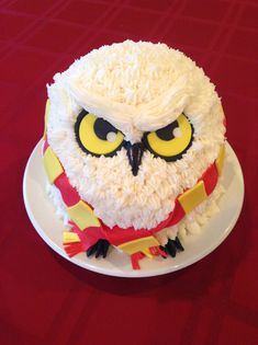 an owl cake with white frosting and yellow eyes is on a red tablecloth